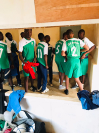 Eine Gruppe junger Fußballspieler in grünen Trikots steht gemeinsam mit einem Trainer vor einem Gebäude in Kamerun und posiert für ein Mannschaftsfoto.